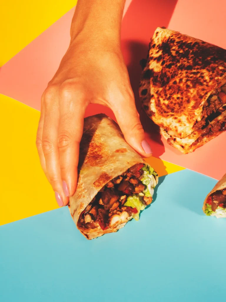 A hand holding a burrito over a colorful placemat